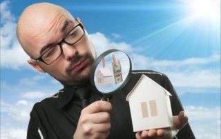 Magnifying glass examining a house model for real estate analysis.