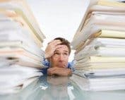 Overwhelmed man surrounded by paperwork and files, stressed with real estate paperwork overload.