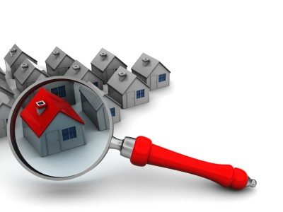 Magnifying glass highlighting a red-roofed house among gray homes, symbolizing real estate focus.