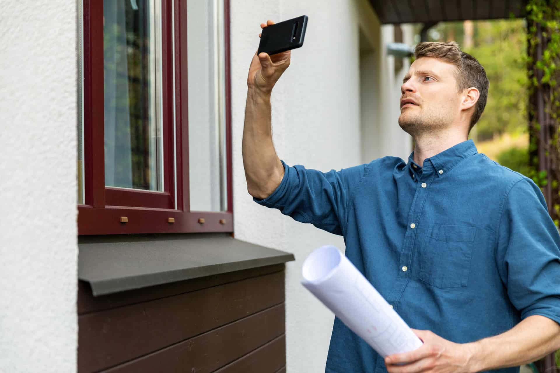 Home appraiser photographing exterior window while holding blueprints during a property inspection in Western Colorado